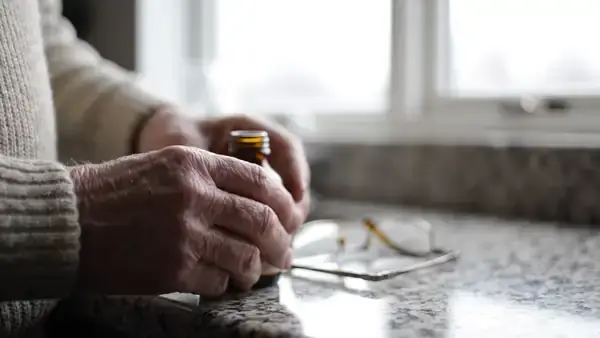 A man's hands turning a small amber bottle around to read the back and setting it down beside reading glasses